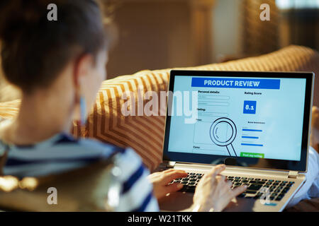 Über die Schulter geschossen der modernen Hausfrau Festlegung auf der Couch in der modernen Haus in sunnny heissen Sommertag schreiben Überprüfung auf Laptop nach Online shopping auf Stockfoto