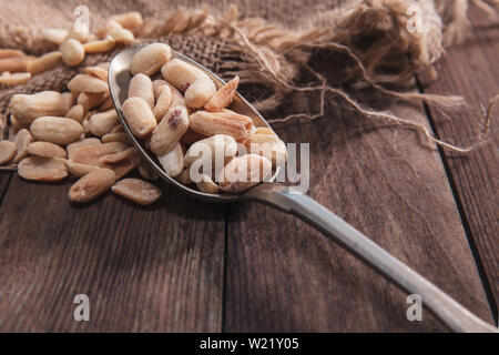 Geröstete Erdnüsse auf einem alten Löffel und Zusammensetzung aus altem Holz und Material. Stockfoto