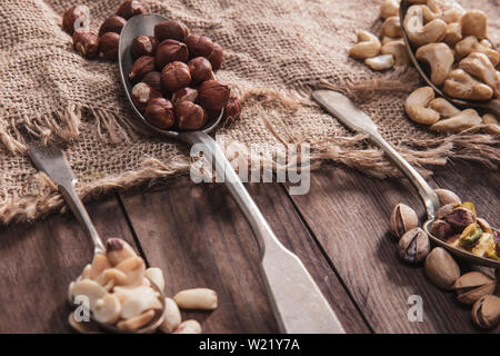 Close-up auf verschiedenen Arten von Nüssen auf alten Löffel und Zusammensetzung aus altem Holz und Material Stockfoto