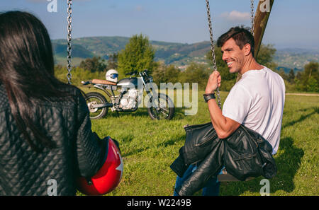 Glückliche junge Mann an ihrer Freundin auf einer Schaukel sitzend auf der Suche Stockfoto