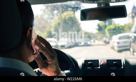 Zurück Blick auf junge Unternehmer fahren Auto und Gespräch am Handy gleichzeitig. Stockfoto