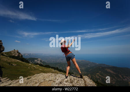 Glückliche Frau in kurzen Shorts und einen Hut tragen, ist das Tanzen auf der Spitze eines Berges. Der Begriff der Freiheit, Freizeit, Reisen. Viel Glück und Erfolg. Stockfoto