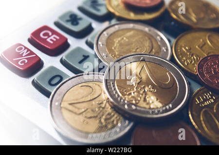 Stapel von 1- und 2-Euro-Münzen mit einem Taschenrechner auf weißem Hintergrund Stockfoto