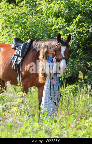 Junge schöne Equestrian Mädchen im Kleid führen Sattel reiten im grünen Wald Stockfoto