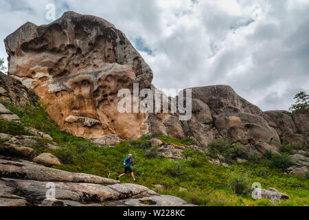 Athlet runner läuft auf einem Höhenweg. Männchen in den Bergen zwischen den Felsen. Mann im blauen Jersey und schwarze Shorts Training im Freien Stockfoto