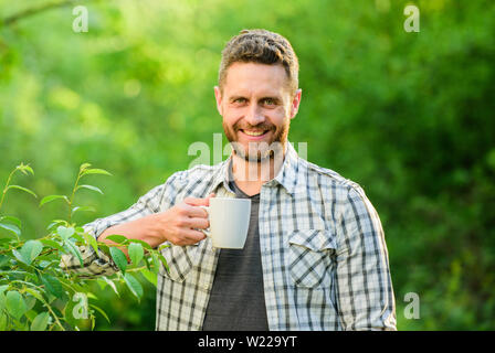 Erfrischendes Getränk. Man bärtige Kaffee Bauer halten Becher Natur Hintergrund. Grüner Tee Plantage. Vollständige blatt Tee. Hervorragender Geschmack. Genießen Sie heiße Getränke. Natürliche trinken. Gesunde Lebensweise. Ich bevorzuge grünen Tee. Stockfoto