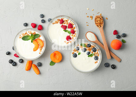 Flach Zusammensetzung mit Joghurt Desserts und Früchten auf grauem Zement Hintergrund Stockfoto