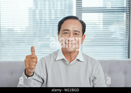 Ältere Mann auf der Couch geben Daumen oben sitzen beim Spielen computer spiel, an der Kamera schaut lächelnd.? Stockfoto