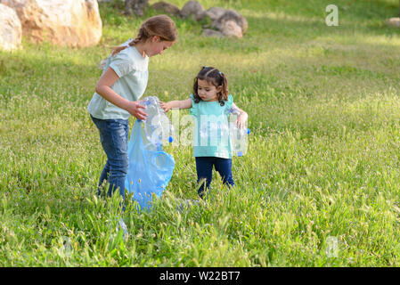 Süße kleine Mädchen Reinigung Kunststoff Wurf auf Gras. Kinder freiwillige Reinigung bis Einstreu und Plastik Flasche in Recycling Tasche. Stockfoto