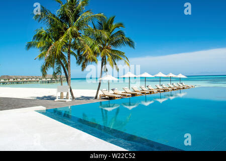 Großen Infinity-pool an der Küste des Indischen Ozeans mit Liegen und Sonnenschirmen im Schatten der Palmen Stockfoto