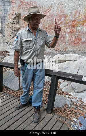 Ein Eingeborener Reiseleiter gibt ein Gespräch auf dem Hintergrund der gut erhaltenen Aboriginal Rock Art Schablone für die Besucher. Die Schablone Art Site wird geglaubt, t Stockfoto