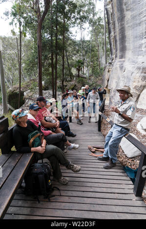 Ein Eingeborener Reiseleiter gibt ein Gespräch auf dem Hintergrund der gut erhaltenen Aboriginal Rock Art Schablone für die Besucher. Die Schablone Art Site wird geglaubt, t Stockfoto