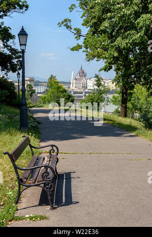 Eine Parkbank entlang eines Weges mit dem ungarischen Parlamentsgebäude im Hintergrund an einem sonnigen Sommertag Stockfoto