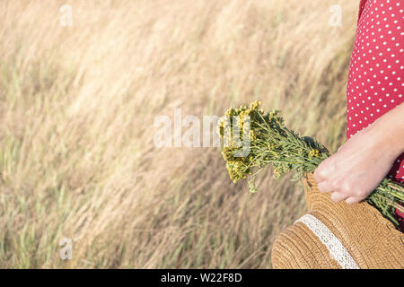 Frau mit einem Blumenstrauß und einem Hut im Feld. Ländliche Szene: Weibliche in Polka-dot-Kleid mit Landwirt hat und Blumenstrauß in der Hand. Stockfoto