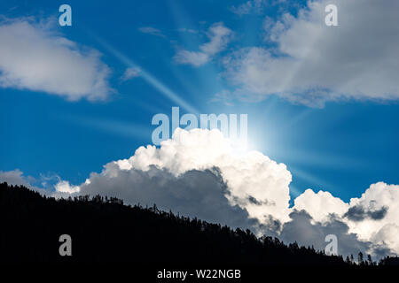 Blauer Himmel mit Wolken und Sonnenstrahlen in Berg, Silhouette eines Waldes. Alpen, Trentino-Südtirol, Italien, Europa Stockfoto