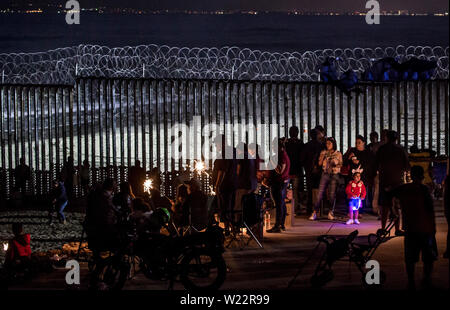 Tijuana, Mexiko. 04. Juli, 2019. Zahlreiche Menschen haben sich die Feuerwerke Leuchten hinter dem Zaun auf der mexikanischen Seite der Grenze Mauer auf US Independence Day. Menschen versammelt, um am Strand des mexikanischen Tijuana die Feiern auf der anderen Seite der Grenze zu beobachten. Credit: Omar Martinez/dpa/Alamy leben Nachrichten Stockfoto