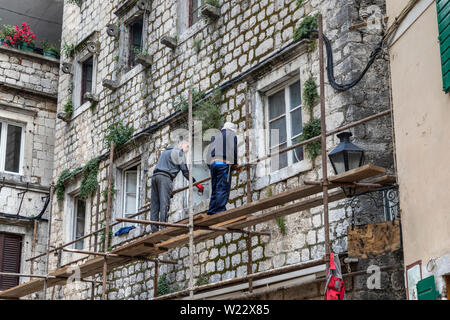 Kotor, Montenegro, 2. Mai 2019: Zwei Arbeiter auf einem Gerüst arbeiten an der vorderen Wand eines alten Gebäude aus Stein Stockfoto