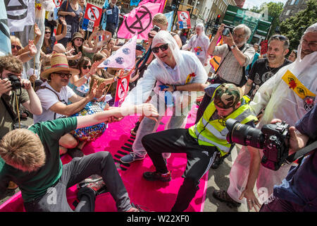 London, Großbritannien. 5. Juli, 2019. Klima Aktivisten vor dem Aussterben Rebellion mime peppersprayed durch die französische Polizei während eines Protestes außerhalb der Französischen Botschaft in Solidarität mit den Mitgliedern des Aussterbens Rebellion Frankreich, die auf kurze Distanz von der französischen Polizei peppersprayed wurden, während die Belegung der Pont de Sully in Paris für weitere Maßnahmen der Regierung und die Aufmerksamkeit der Medien auf den Klimawandel zu nennen. Credit: Mark Kerrison/Alamy leben Nachrichten Stockfoto