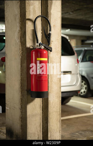Feuerlöscher an der Wand auf einem Parkplatz mit Autos hung Stockfoto