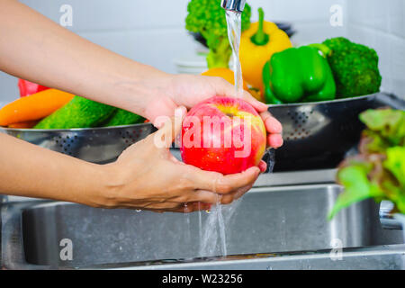 Junge Frau Waschen von Salat und Äpfel Pestizide vor dem Kochen in der Küche entfernen. Obst und Gemüse Konzept waschen. Stockfoto