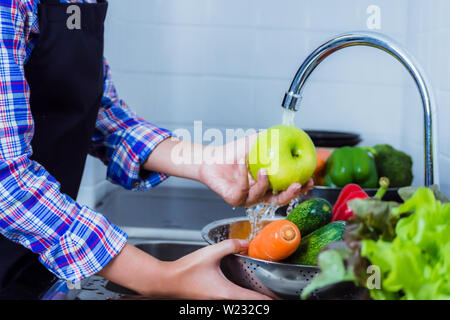 Junge Frau Waschen von Salat und Äpfel Pestizide vor dem Kochen in der Küche entfernen. Obst und Gemüse Konzept waschen. Stockfoto