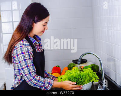 Junge Frau Waschen von Salat und Äpfel Pestizide vor dem Kochen in der Küche entfernen. Obst und Gemüse Konzept waschen. Stockfoto