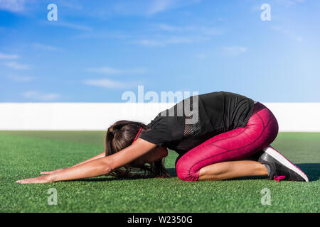 Yoga asiatische Frau tun Zurück erstreckt sich ausdehnenden Übungen namens childs stretch Pose mit ausgestreckten Armen für Gesundheit und Körper Flexibilität auf Gras, der Außenpool im Sommer Fitness Gym. Stockfoto