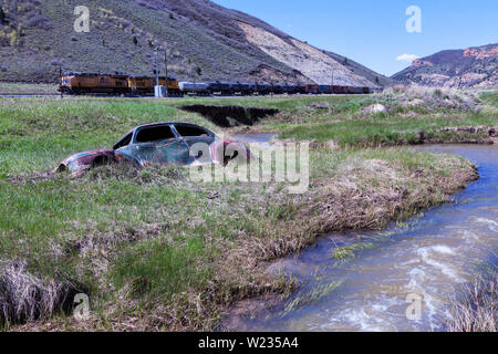 Ein bullet enträtselt 1946 Plymouth Deluxe teilweise in den Creek Bed von Echo Creek in Echo Canyon eingetaucht ist als Union Pacific freight Köpfe gen Osten. Stockfoto