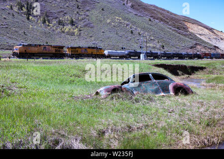 Ein bullet enträtselt 1946 Plymouth Deluxe teilweise in den Creek Bed von Echo Creek in Echo Canyon eingetaucht ist als Union Pacific freight Köpfe gen Osten. Stockfoto