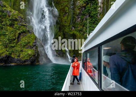 Einen Milford Sound Cruise Boot nähert sich einem Wasserfall, Fiordland National Park, South Island, Neuseeland Stockfoto