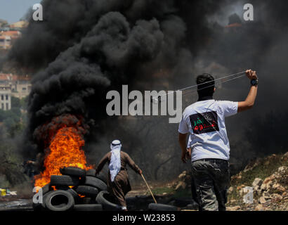 Juli 5, 2019 - Qalqilia, Palästina. 05. Juli 2019. Palästinenser Demonstranten Konfrontation mit israelischen Soldaten im Westjordanland Stadt Kafr Qaddum während ihrer wöchentlichen Freitag Protest gegen illegalen israelischen Siedlungen. Einige Palästinenser verbrannten Reifen und warfen Steine auf die israelischen Streitkräfte, die befeuerte Gas und mit Gummi überzogene Kugeln auf Demonstranten und verletzte mindestens vier von ihnen reißen. Seit Juli 2011, Bewohner von Kafr Qaddum und den benachbarten Dörfern organisieren Proteste am Freitag gegen die Verlängerung der nahe gelegenen israelischen Siedlung Qadumim, die Schließung der Palästinenser des Dorfes ma Stockfoto