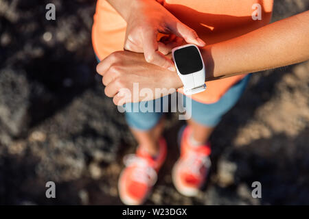 Trail Runner Athlet mit Ihrem smart Watch App fitness Fortschritt oder Herzfrequenz während Run cardio Workout zu überwachen. Frau Training im Freien auf Felsen. Nahaufnahme von Tech Gear. Stockfoto