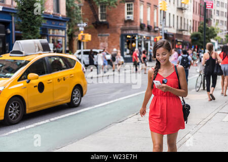 Frau zu Fuß in New York City mit Phone App für Taxifahrt hageln Service oder online spielen Spiel beim Pendeln von der Arbeit. Asiatische Mädchen touristische Suche nach Karte Wegbeschreibung auf dem Smartphone. Stockfoto