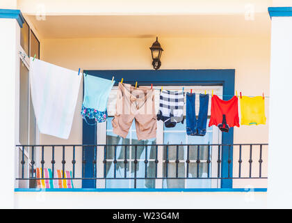 Kleidung hängend auf einer Wäscheleine auf einem hellen, modernen Stil in Blau und Weiß. Es gibt einen attraktiven Metallbarriere Zaun vor und ein Fenster wi Stockfoto