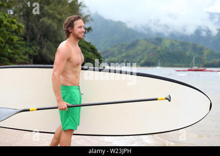 Stand Up Paddle Board Strand Mann tun paddleboarding Paddleboard gehen in Hawaii. Junge kaukasier männlichen Athleten auf Hawaiian Beach auf Sommerferien urlaub reisen. Stockfoto