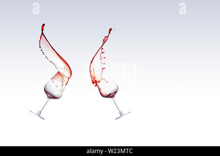 Zwei Gläser Rotwein mit dem Wein das Herausspritzen von einem Glas, auf weißem Hintergrund Stockfoto