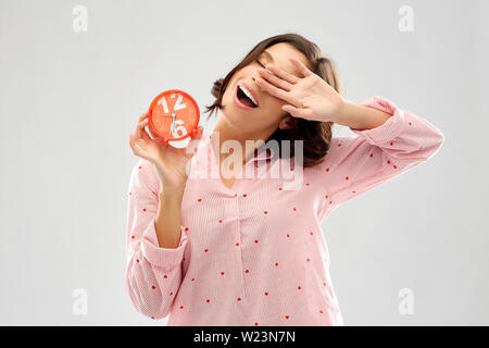Verträumte junge Frau im Pyjama mit Wecker Stockfoto