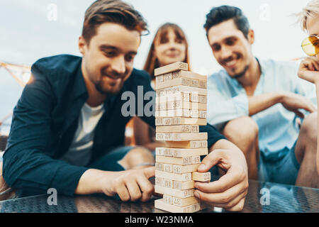 Die Gesellschaft junger Menschen jenga spielen. Junge Freunde bei Sonnenuntergang auf Penthouse Terrasse jenga spielen Stockfoto