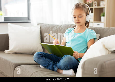 Mädchen in Kopfhörer mit Tagebuch auf dem Sofa zu Hause Stockfoto