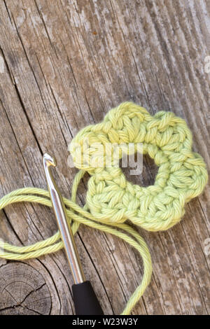 Gewirken gelbe Blüte mit Häkelnadel und Wolle auf hölzernen tablel Stockfoto