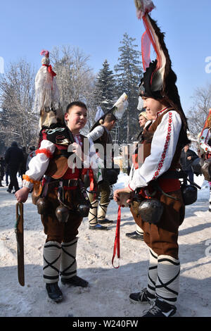 Razlog, Bulgarien - 12. Januar 2019: Zwei in bulgarischen Volkstrachten gekleidete Jungen auf der verschneiten Straße beim Volksfest in Starchevata und Maskerade Stockfoto