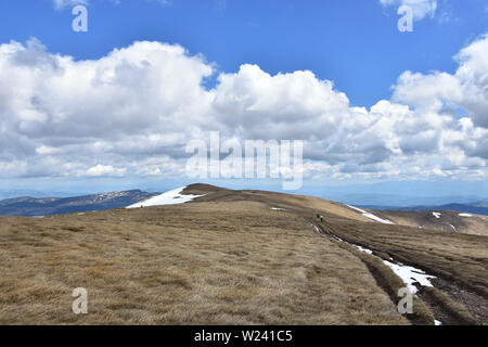 Späte Quelle auf dem Hochgebirge in der Nähe des Ruen Peak, des Osogovo Mountain. Zwei Menschen gehen in der Ferne auf die Straße Stockfoto