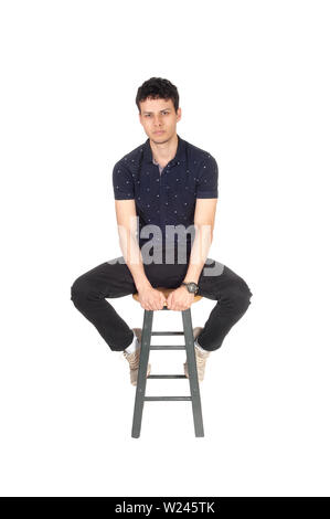 Ein gut aussehender junger Mann in schwarzer Kleidung auf einem Stuhl sitzen im Studio, Ausruhen, bei weißem Hintergrund Stockfoto