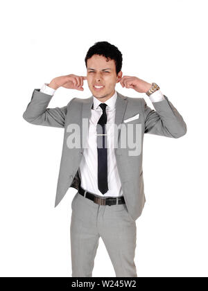 Eine verärgerte junge Unternehmer stehen in einem grauen Anzug seine Finger in seine Ohren, Dos nicht gerne hören, auf weißem Hintergrund Stockfoto