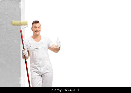 Maler mit einem Farbroller lehnte sich gegen die Wand und einen Daumen nach oben Zeichen auf weißem Hintergrund Stockfoto