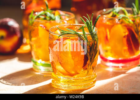 Gläser mit Tropfen süßen Pfirsich Eistee, Sommer kalt Pfirsich fizz Cocktail mit Rosmarin. Sonnigen Licht. Geringe Tiefe des Feldes, Nahaufnahme, kopieren Spa Stockfoto