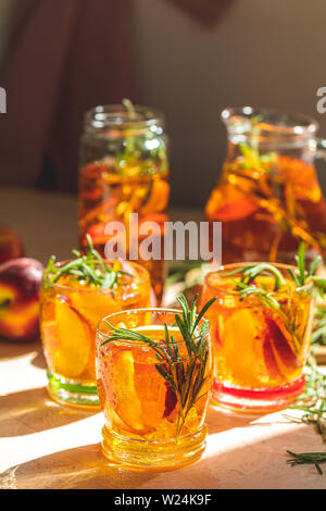 Gläser mit Tropfen süßen Pfirsich Eistee, Sommer kalt Pfirsich fizz Cocktail mit Rosmarin. Sonnigen Licht. Geringe Tiefe des Feldes, Nahaufnahme, kopieren Spa Stockfoto