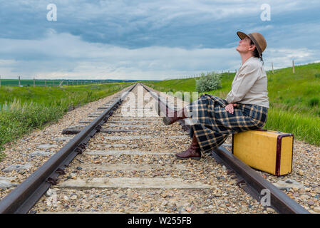 Junge Frau in historischen Kleid sitzt auf vintage Koffer auf Bahnstrecke nach oben geschaut - Reise Konzept Stockfoto