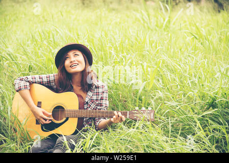 Schöne junge Frau, die Gitarre spielen auf der grünen Wiese. Stockfoto