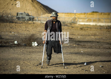 Gaza, Palästina. 05. Juli, 2019. Eine palästinensische Demonstrator Spaziergänge auf seine Krücken auf den Grenzzaun während einer Demonstration für ein Ende der Belagerung des Gazastreifens im südlichen Gazastreifen verhängt. Credit: SOPA Images Limited/Alamy leben Nachrichten Stockfoto